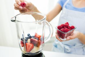 woman putting berries and banana in a blender